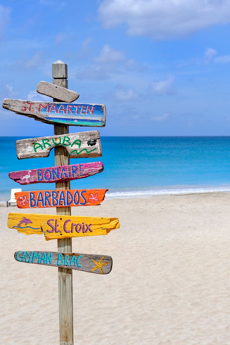 a sign on the beach pointing to different caribbean islands